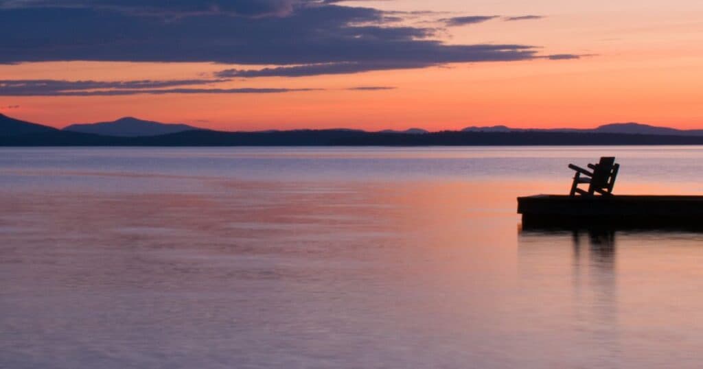 Adirondack chair at the end of a quiet pier overlooking calm water at sunset, symbolizing peace and reflection in the final days of life.