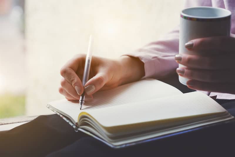hand writing journal tea person's hand writing in journal with cup of tea